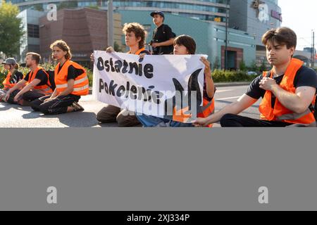 15 luglio 2024, Varsavia, Polonia: Al centro della cornice, gli attivisti tengono uno striscione che dice: '' Ostatnie Pokolenie'' durante la manifestazione. Le persone in giubbotti arancioni (attivisti dell'ultima generazione) hanno bloccato il traffico su Aleja Jana Pawla II. Si tratta di attivisti dell'ultima generazione che chiedono investimenti nel trasporto pubblico. L'ultima generazione ha bloccato le principali arterie di Varsavia per la terza settimana. L’ultima generazione ha dichiarato davanti alle telecamere: Non ci fermiamo, il nostro obiettivo è la più lunga serie di azioni di resistenza civile contro il crollo climatico in Polonia. Nella stagione più calda, pe Foto Stock