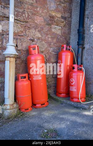 Bombole di gas rosso brillante, bombole di gas in piedi contro un muro in una strada, di Calor gas Ltd. Warwick; alcuni collegati da tubi Foto Stock