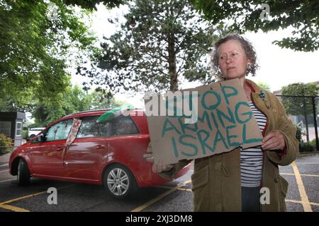 Bristol, Inghilterra, Regno Unito. 15 luglio 2024. Un sostenitore degli attivisti ha un cartello che dice "˜ smettila di armare Israele" fuori dalla fabbrica. Per due giorni consecutivi gli attivisti hanno bloccato la strada che porta alla fabbrica di Elbit Systems impedendo ai lavoratori di frequentare i loro uffici. I sostenitori di Palestine Action usano i lock-on per rendere la loro rimozione più difficile e dispendiosa in termini di tempo ad Aztec West, Bristol. Essi sostengono che le armi prodotte da Elbit nel Regno Unito sono usate dagli israeliani contro i palestinesi a Gaza e altrove. I bombardamenti israeliani a Gaza hanno ucciso oltre 35.000 palestinesi da ottobre Foto Stock