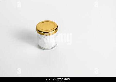 Cristalli di mentolo in vasetto di vetro piccolo su tavolo bianco. Spazio di copia vuoto. Berretto d'oro, rimedio naturale. Grado alimentare naturale puro. Raffreddamento e freschezza Foto Stock