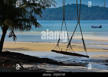 Un'altalena rustica di corda in legno su una spiaggia di sabbia tropicale con una barca nel mare turchese, Koh Rong Sanloem, Cambogia Foto Stock