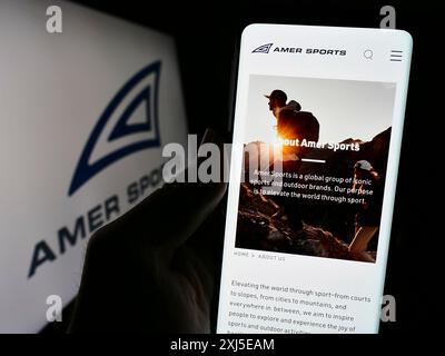 Stoccarda, Germania, 02-15-2024: Persona che detiene il cellulare con pagina web della società finlandese di attrezzature sportive Amer Sports Oyj davanti al logo. Concentrati Foto Stock