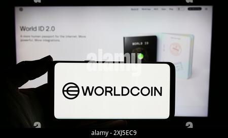 Stoccarda, Germania, 02-15-2024: Persona con smartphone con logo del progetto di criptovaluta Worldcoin (Tools for Humanity) davanti al sito web. Foto Stock