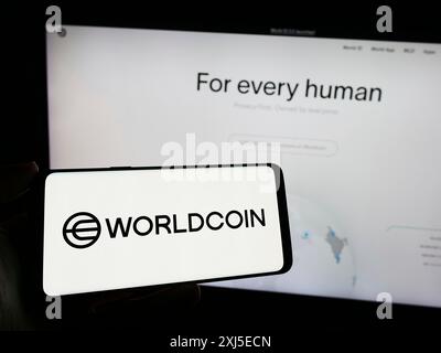 Stoccarda, Germania, 02-15-2024: Persona che tiene un cellulare con il logo del progetto di criptovaluta Worldcoin (Tools for Humanity) di fronte all'azienda Foto Stock