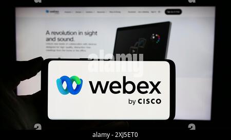 Stoccarda, Germania, 02-19-2024: Persona che detiene un telefono cellulare con il logo della società americana di comunicazioni unificate Webex by Cisco davanti alla pagina web. Foto Stock