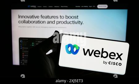Stoccarda, Germania, 02-19-2024: Persona che possiede uno smartphone con il logo della società statunitense di comunicazioni unificate Webex by Cisco davanti al sito Web. Concentrati su Foto Stock