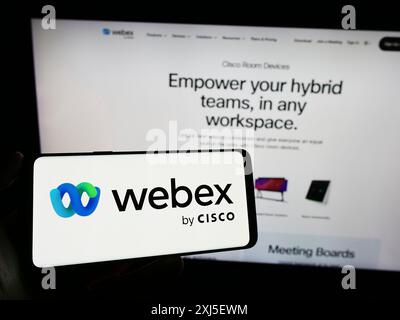 Stoccarda, Germania, 02-19-2024: Persona che detiene un cellulare con il logo della società statunitense di comunicazioni unificate Webex by Cisco di fronte alla pagina Web aziendale. Foto Stock