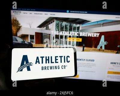 Stuttgart, Germania, 02-22-2024: Persona che possiede uno smartphone con il logo della società statunitense di bevande Athletic Brewing Company davanti al sito Web. Concentrati su Foto Stock