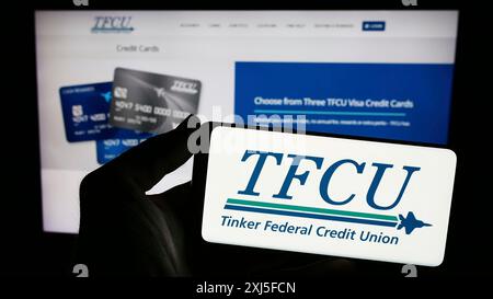 Stoccarda, Germania, 02-22-2024: Persona che detiene lo smartphone con il logo della società finanziaria statunitense Tinker Federal Credit Union (TFCU) davanti al sito web. Foto Stock