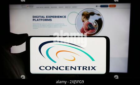 Stoccarda, Germania, 02-21-2024: Persona che detiene un cellulare con il logo della società statunitense di servizi alle imprese Concentrix Corporation davanti all'azienda Foto Stock