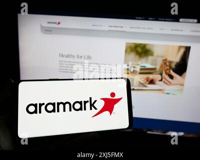 Stoccarda, Germania, 02-22-2024: Persona che detiene un cellulare con il logo della società americana di servizi alimentari e di gestione delle strutture Aramark di fronte Foto Stock