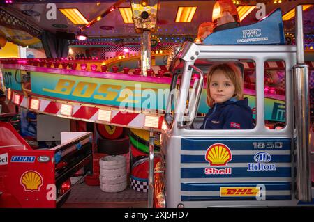 Ragazzo, 5 anni, biondo, in giostra per bambini, giostra, logo, Bose, Shell, Hilton, DHL, IWC Schaffhausen, Fiat, fiera, festival primaverile, folk Foto Stock