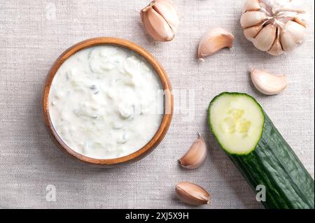 Tzatziki fresco in una ciotola di legno su tessuto di lino. Salsa rinfrescante, zuppa o salsa, fatta di yogurt affaticato salato, mescolato con cetrioli, aglio, ecc. Foto Stock