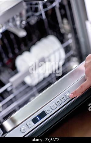 La mano della donna si accende in lavastoviglie per lavare i piatti. Elettrodomestici incorporati in cucina Foto Stock