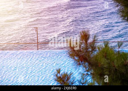 Vista accattivante di un tranquillo paesaggio marino mediterraneo al tramonto, caratterizzato da una superficie d'acqua scintillante e lussureggianti pini costieri, perfetto per i viaggi Foto Stock