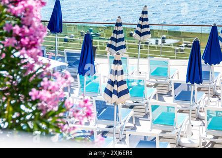 Un'invitante terrazza sul mare con file di lettini turchesi abbinati a eleganti ombrelloni a righe blu e bianche. Elegante relax Foto Stock