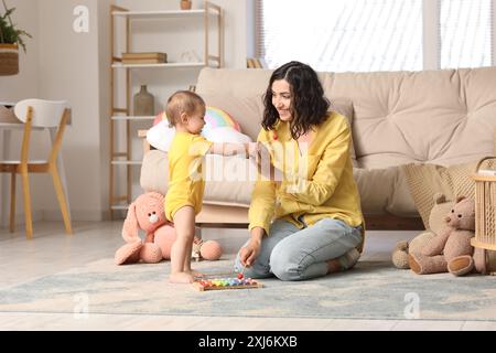 Bella, giovane, felice madre e piccolo bambino che gioca con lo xilofono a casa Foto Stock