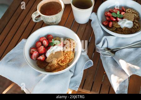 Primo piano di due colazioni in terrazza con pancake, fragole, panna, burro di arachidi e tè Foto Stock