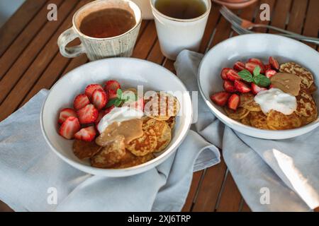 Primo piano di due colazioni in terrazza con pancake, fragole, panna, burro di arachidi e tè Foto Stock