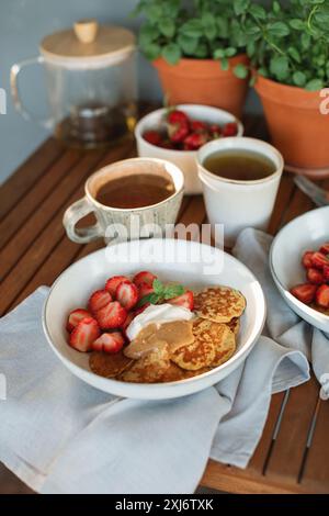 Primo piano di una colazione in terrazza con pancake, fragole, panna, burro di arachidi e tè Foto Stock