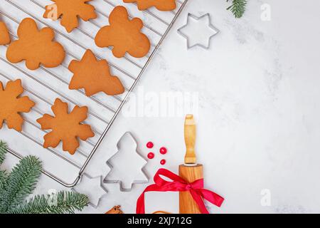 Un ambiente festivo con biscotti di pan di zenzero appena sfornati in varie forme su una griglia di raffreddamento. Tronchesini per biscotti e un mattarello con un nastro rosso Foto Stock