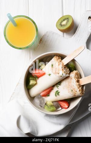 Frutta pop di ghiaccio con fragola e kiwi nella ciotola sul tavolo con succo di arancia Foto Stock