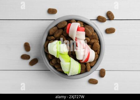 Cibo e dolcetti per cani secchi (ossa da masticare annodate) su pavimento di legno bianco, piano Foto Stock