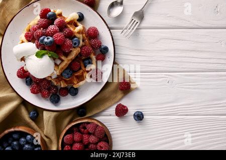 Vista superiore del pane appena sfornato cialde belghe con frutti di bosco e gelato su bianco tavolo in legno Foto Stock