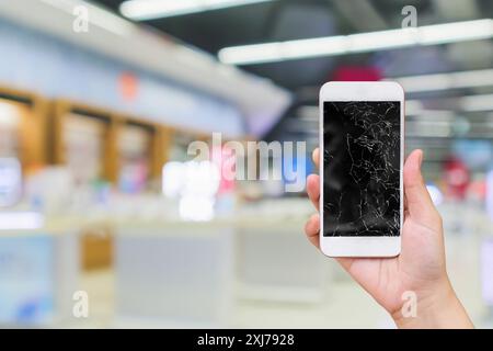 tenere a mano il telefono cellulare con schermo in vetro rotto e negozio elettronico di sfocatura astratta per la riparazione dello smartphone Foto Stock