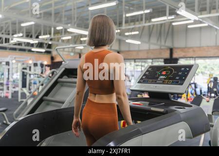 Vista posteriore di una giovane donna che cammina sul tapis roulant durante l'esercizio mattutino in palestra Foto Stock