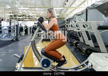 Giovane donna che usa la macchina da coaster ab durante il suo esercizio mattutino in una palestra locale Foto Stock