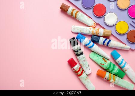 Un variopinto assortimento di pastelli e pennelli sono disposti su uno sfondo rosa. I pastelli sono di vari colori e dimensioni e i pennelli Foto Stock