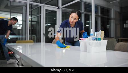 Detergente, donna e tavolo di pulizia ufficio per fumigazione, spray disinfettare e tuta di sicurezza dal rischio di malattia nell'edificio. Manutenzione, persona e. Foto Stock