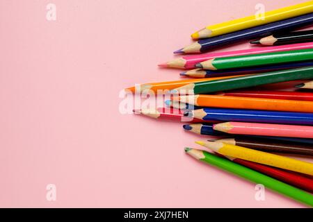 Una fila di matite colorate su sfondo rosa. Le matite sono disposte in modo che siano tutte rivolte nella stessa direzione, creando un senso di corda Foto Stock