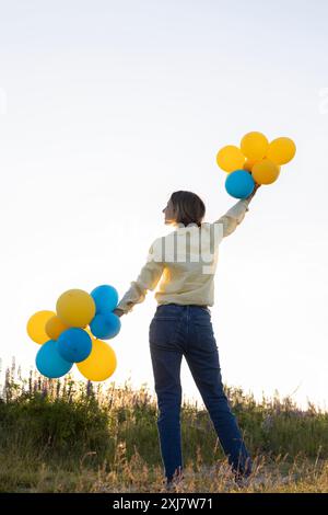 la donna felice si erge contro il cielo, tenendo in mano molti palloncini gialli e blu. Il giorno della mongolfiera. Compleanno. Sogni di pace per l'Ucraina. Io sono orgoglioso Foto Stock