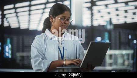 Ritratto di un responsabile del dipartimento di ingegneria del software tecnologico che sta in piedi e utilizza un computer portatile. Donna indiana si è concentrata sul pensiero mentre lavorava in ufficio Foto Stock