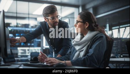 Due diversi colleghi indiani multietnici che hanno una conversazione mentre sono impegnati a lavorare a un progetto di sviluppo software. Engneer donna che parla con un Project Manager. Lavoro di squadra nel laboratorio tecnologico Foto Stock