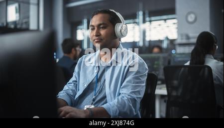 Amministratore di sistema indiano che lavora in una struttura di e-Business di ricerca su un computer desktop. Sviluppatore di software specializzato in abiti casual che indossano cuffie e aggiornano il database del sistema server Foto Stock