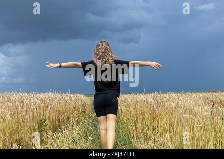 donna irriconoscibile con braccia allungate si erge in un campo di grano maturo e asciutto. La bellezza della natura. Energia terrestre. buon raccolto. La val Foto Stock