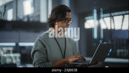 Ritratto di un responsabile del dipartimento di ingegneria del software tecnologico che sta in piedi e utilizza un computer portatile. Donna indiana si è concentrata sul pensiero mentre lavorava in ufficio Foto Stock
