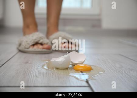 Donna vicina a un uovo crudo rotto su un pavimento in legno grigio in interni, messa a fuoco selettiva. Spazio per il testo Foto Stock