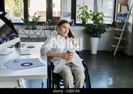 Una giovane donna d'affari con disabilità siede su una sedia a rotelle in un ufficio moderno e fa una telefonata. Foto Stock