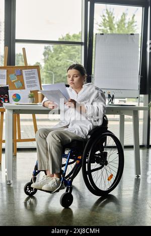 Una giovane donna d'affari in sedia a rotelle siede a una scrivania in un ufficio moderno per rivedere i documenti. Foto Stock