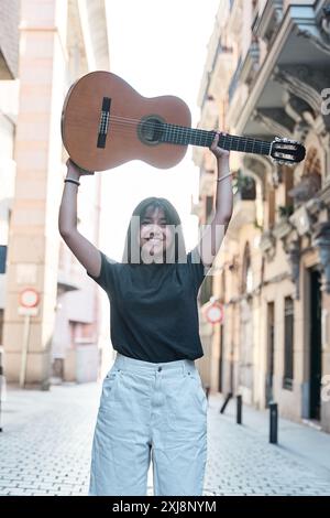 ritratto verticale di una giovane donna latina che solleva una chitarra classica sopra la testa Foto Stock