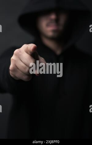 Oscuro, criminale e uomo in studio, che punta e si nasconde sotto copertura per stalking, persona e ladro con il crimine. Sfondo nero, truffa e nascondersi con la felpa con cappuccio Foto Stock