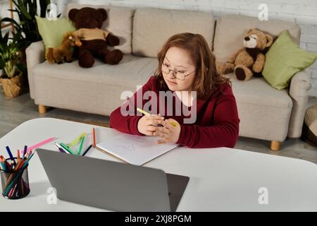 Una bambina con la sindrome di Down siede a un tavolo, colorando in un taccuino. Foto Stock