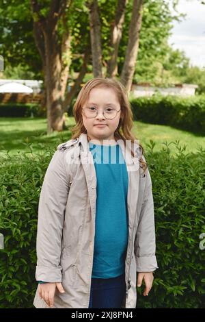 Una bambina con la sindrome di Down si trova nel suo cortile, circondata da alberi e cespugli verdi. Foto Stock