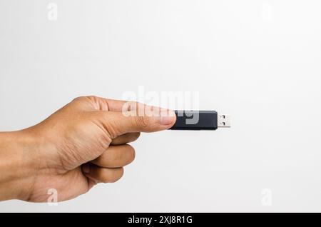 Mano di un uomo che tiene in mano un'unità flash USB nera con la punta delle dita isolata su sfondo bianco. Foto Stock