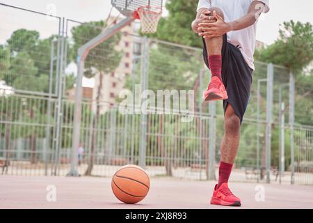 Giovane cestista afroamericano irriconoscibile che si allunga le gambe prima di giocare Foto Stock