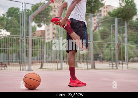 Giovane cestista afroamericano irriconoscibile che si allunga le gambe prima di giocare Foto Stock